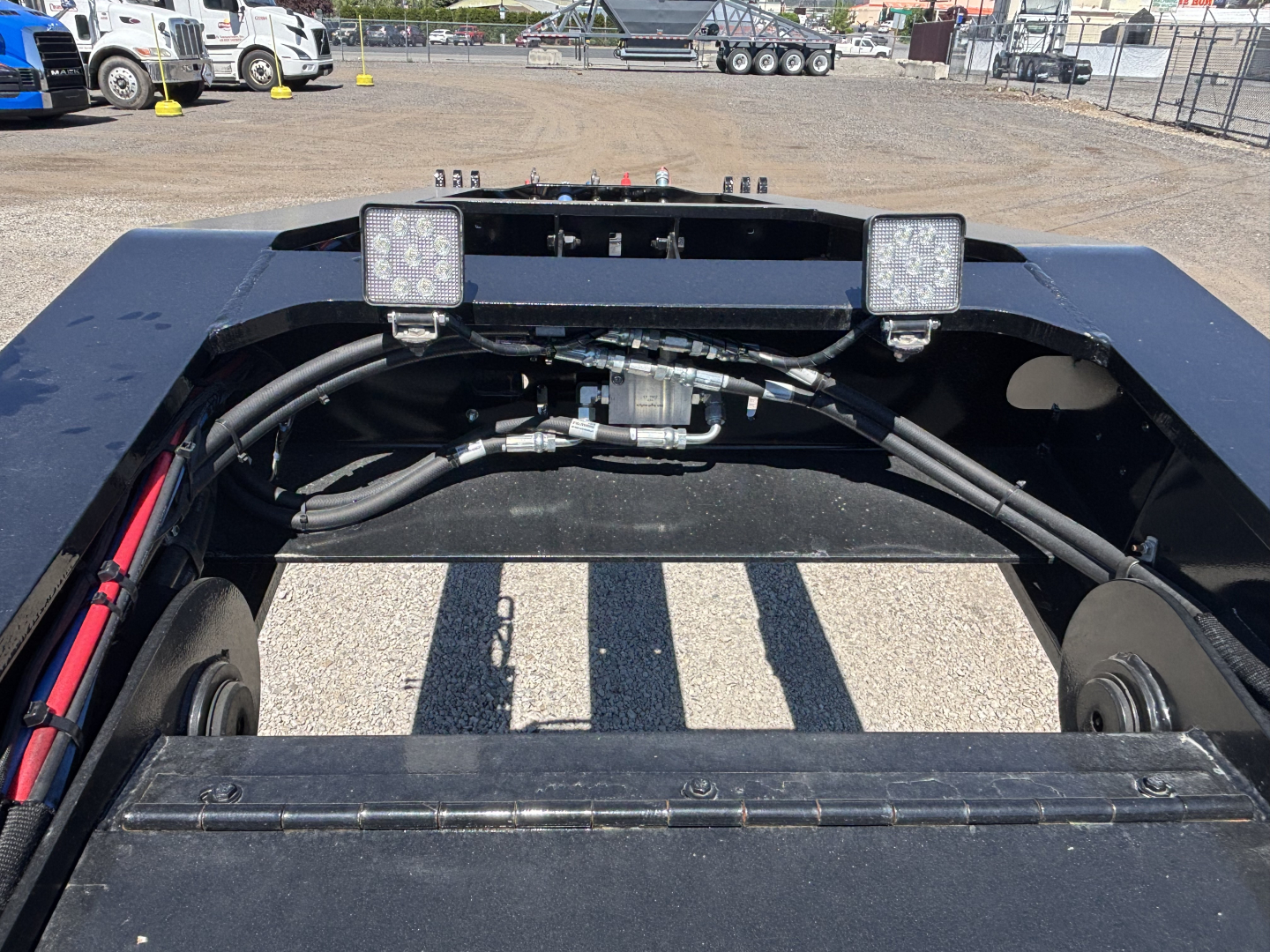 Trailer chassis view showing hydraulic lines and wiring harness with two square LED work lights mounted on frame.