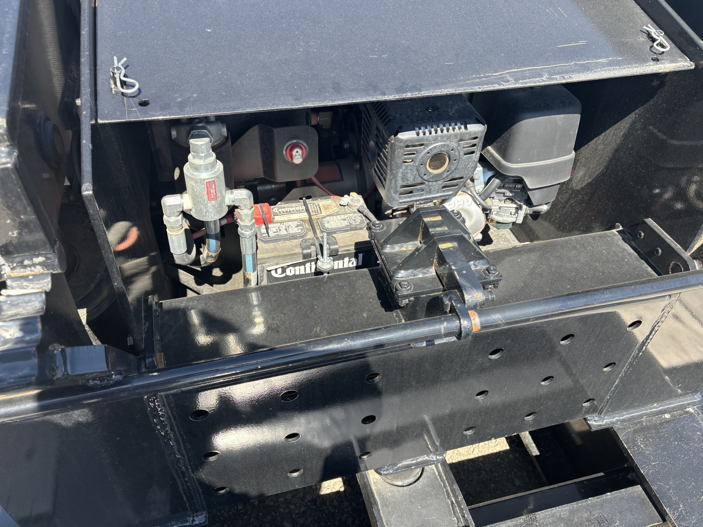 Trailer engine bay showing battery, starter, and hydraulic/electrical components with wiring and metal brackets.