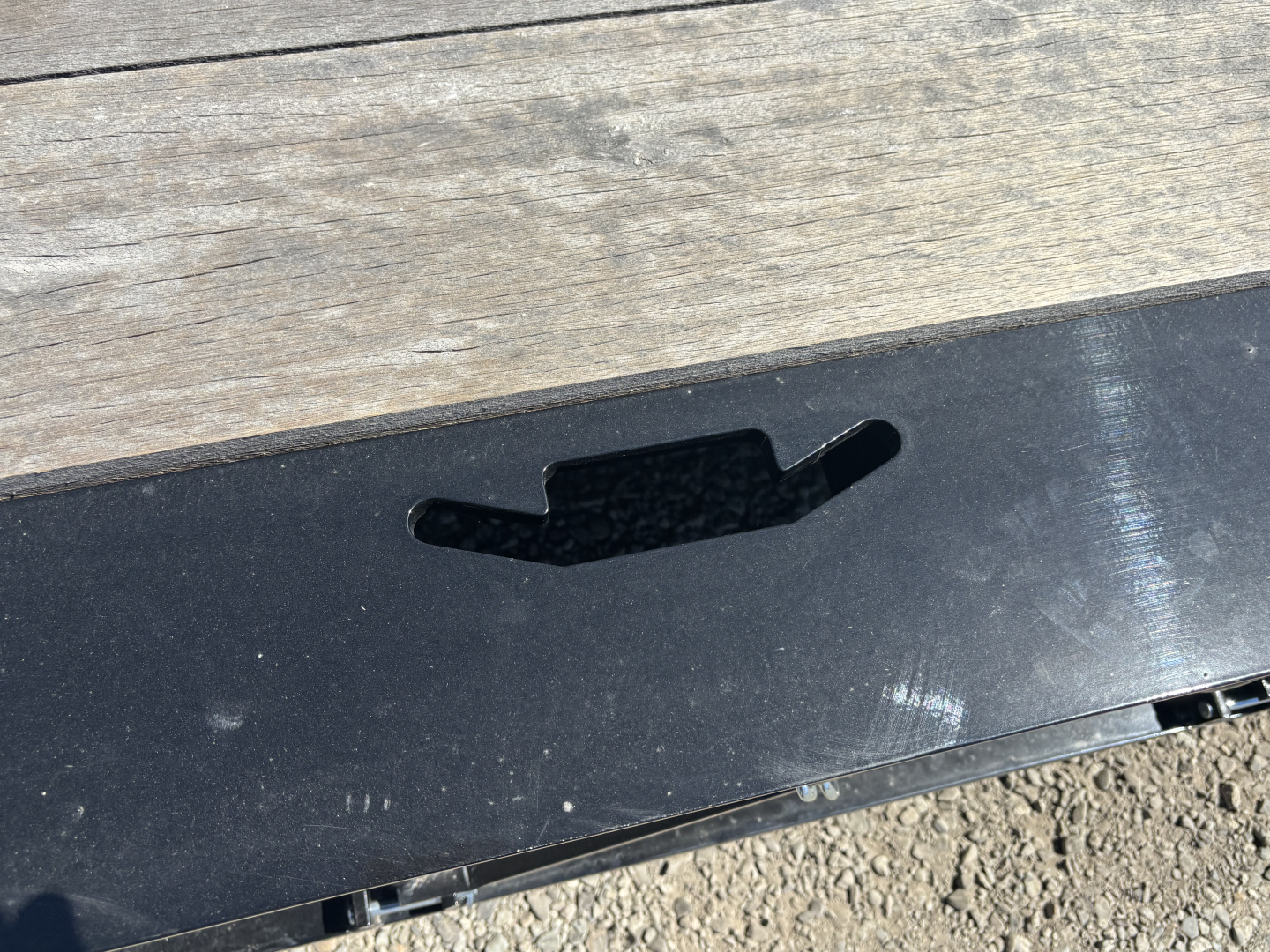 Lowboy trailer edge with slot and black metal surface showing cutout and wooden deck in background.