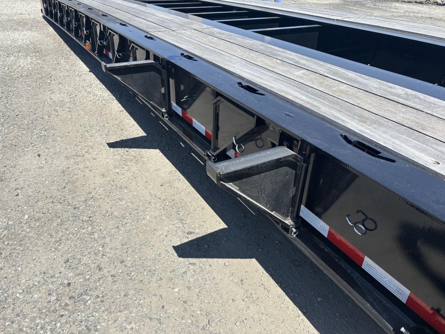 Lowboy trailer side view showing steel deck and undercarriage with reflective tape and recessed steps.