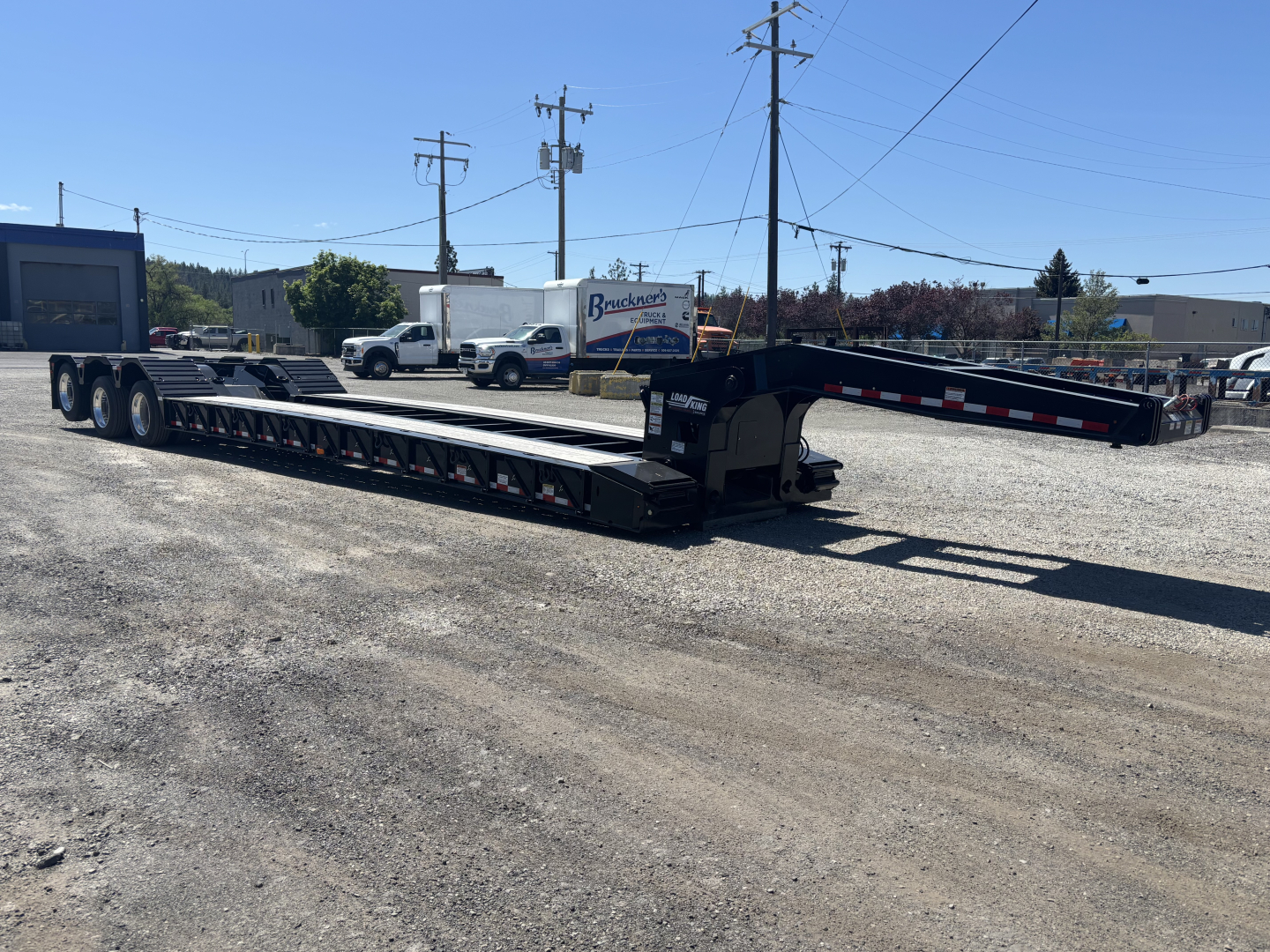 Load King lowboy trailer showing dual-deck extendable sections with gooseneck and ramps extended, black with reflective markings.