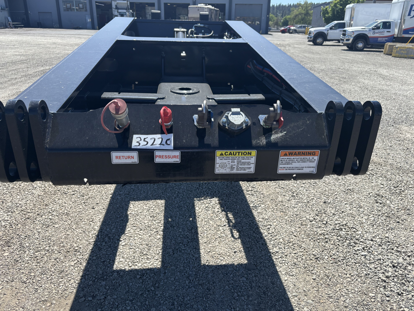 Trailer hitch area of a Load King lowboy trailer showing hydraulic coupler and warning labels, with red/tan knobs and a Caution label visible.