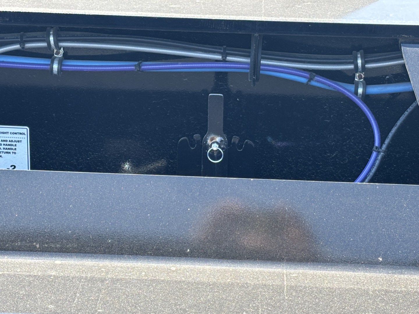 Trailer hitch area showing a lifting ring/hook mounted on a Load King lowboy trailer with blue wiring harness and metal frame.