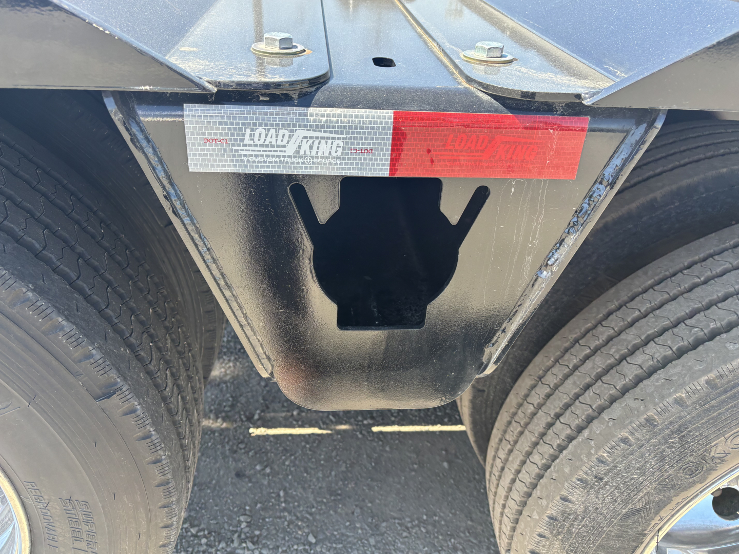 Load King trailer frame showing axle cutout and stickers: LOAD KING logo and red safety label, dual tires visible.