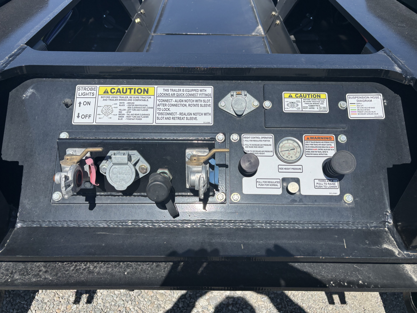 Trailer controls panel showing two toggle switches, multiple warning labels, and gauge dials on a Load King lowboy trailer.