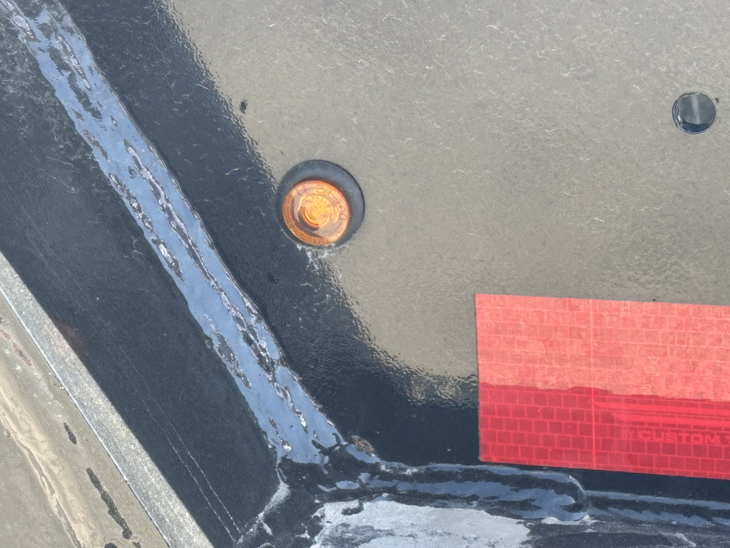 Trailer corner showing black painted surface with orange side marker light and a red reflective tape, part of Load King lowboy trailer body.