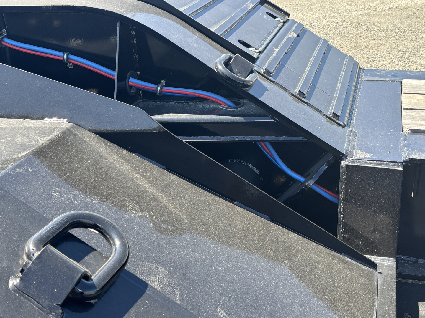 Trailer deck area showing black steel frame with electrical wiring harnesses and a metal step; blue and red wires run along the frame.
