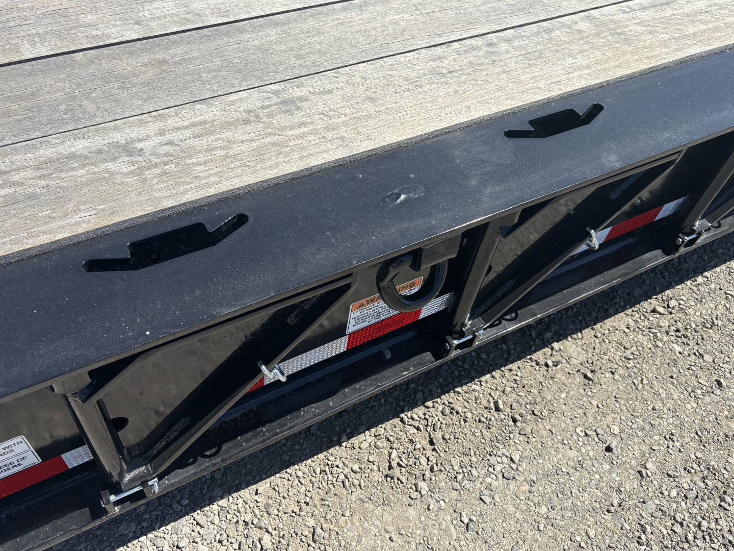 Trailer deck edge with black metal frame and triangular bracing, warning label and reflective tape along bottom.