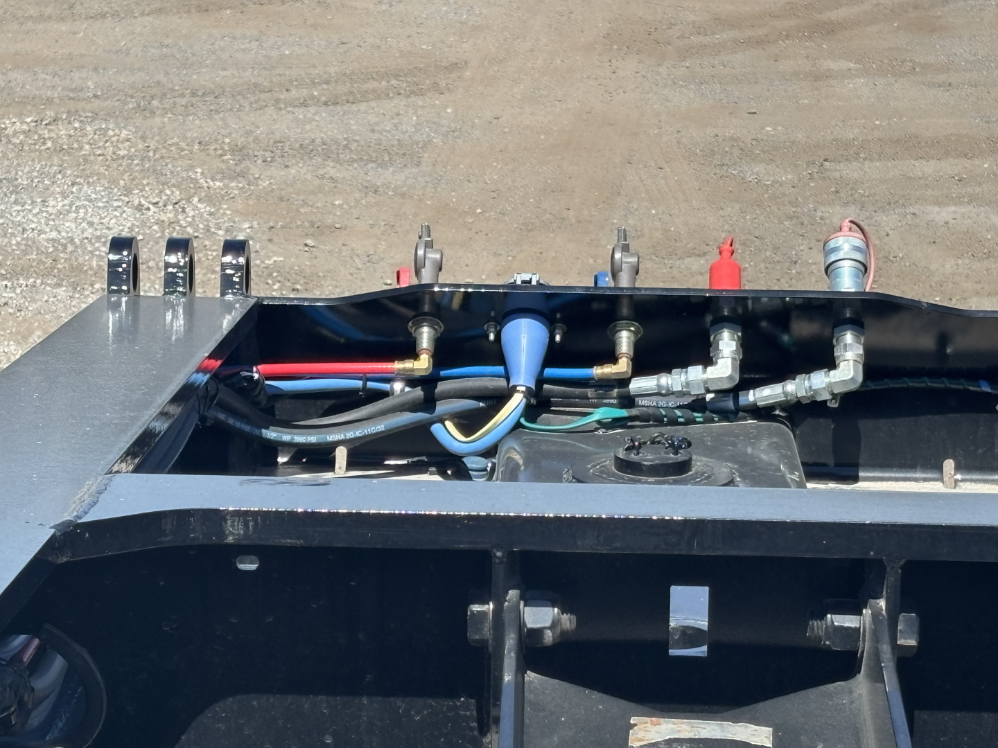 Trailer top view showing hydraulic hoses, fittings, and control components on a Load King trailer with blue fitting and various metal brackets.
