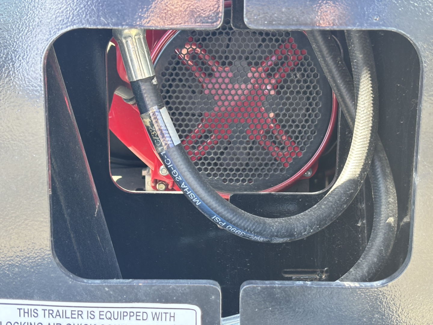 Trailer engine-like component visible through opening: black housing, red cross-brace, thick hoses/leads, circular grille with red X pattern behind.