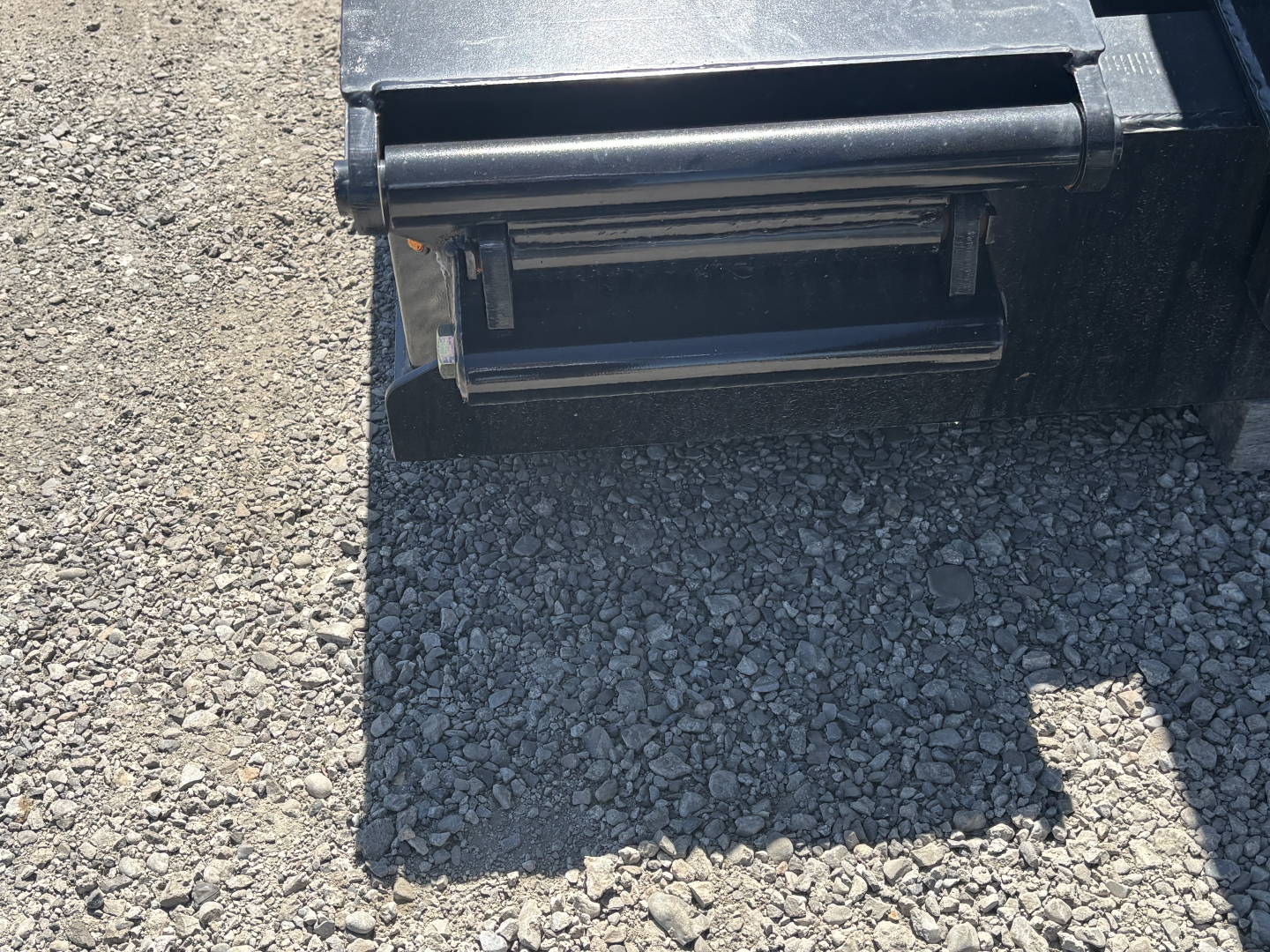 Trailer hitch/step area with rectangular fold-out ladder-like step at rear, on gravel ground.