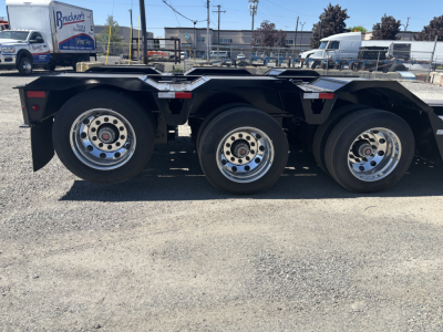 Trailer axle section showing three axles with chrome wheels and black frame, Load King 9' x 24' lowboy trailer in view.