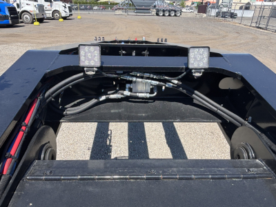 Trailer chassis view showing hydraulic lines and wiring harness with two square LED work lights mounted on frame.