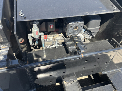 Trailer engine bay showing battery, starter, and hydraulic/electrical components with wiring and metal brackets.