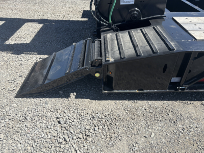 Trailer rear view showing fold-down ramp with textured steps on a Load King lowboy trailer, black steel, gravel surface.