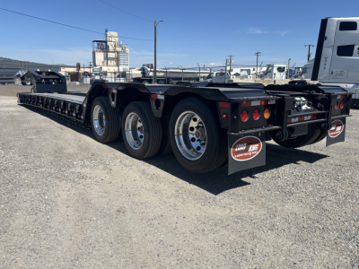 Load King lowboy trailer showing triple-axle rear and long deck with tag lights and mudflaps.
