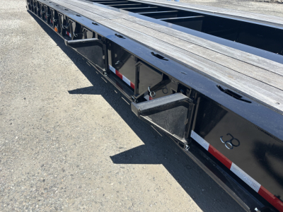 Lowboy trailer side view showing steel deck and undercarriage with reflective tape and recessed steps.