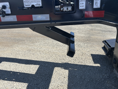 Trailer hitch area of a Load King lowboy trailer showing a support leg and hydraulic mechanism with warning labels and reflective tape.