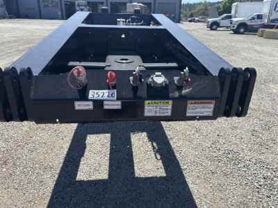 Trailer hitch area of a Load King lowboy trailer showing hydraulic coupler and warning labels, with red/tan knobs and a Caution label visible.