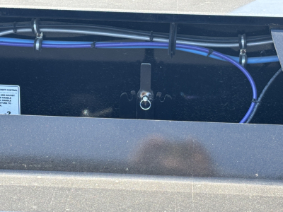 Trailer hitch area showing a lifting ring/hook mounted on a Load King lowboy trailer with blue wiring harness and metal frame.