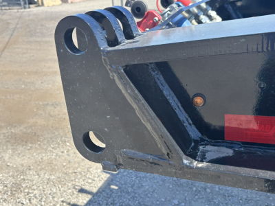 Load King trailer hardware showing welded steel frame with rounded mounting holes and reinforced bracket. Visible label area and blue hydraulic components in background.
