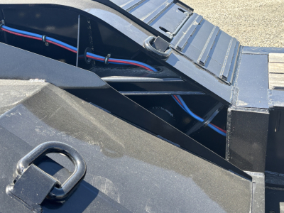 Trailer deck area showing black steel frame with electrical wiring harnesses and a metal step; blue and red wires run along the frame.