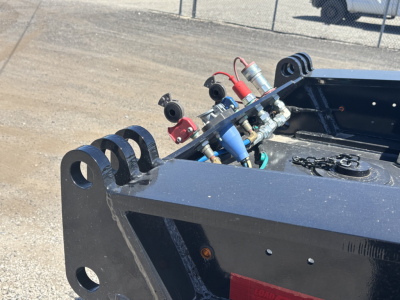 Load King trailer hitching hardware and hydraulic components on a flatbed trailer bed, with blue hydraulic lines and fittings visible.
