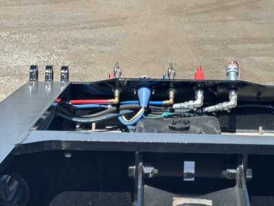 Trailer top view showing hydraulic hoses, fittings, and control components on a Load King trailer with blue fitting and various metal brackets.