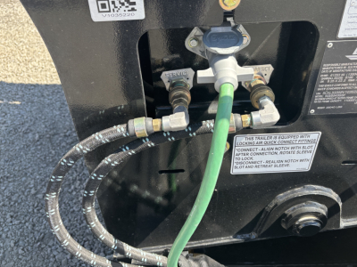 Trailer back showing hydraulic kingpin and connections: green hose connected to relief valve, braided hose with metal fittings, service and lock labels.