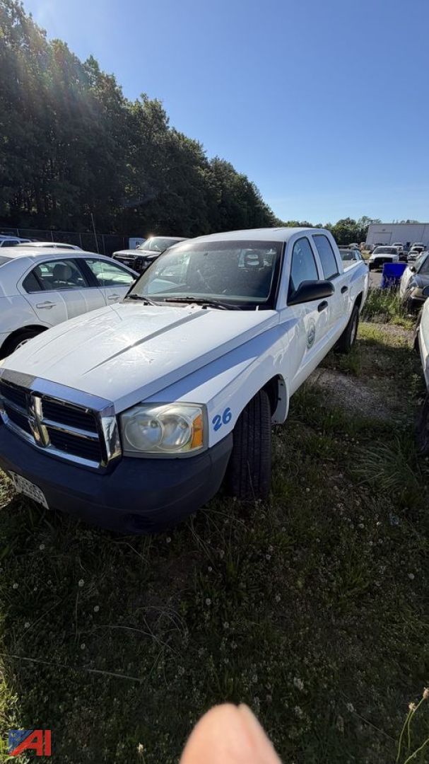 Dodge Dakota pickup truck in a used lot, white with blue accents, front left angle, number 26 on fender, outdoors with other vehicles in background.
