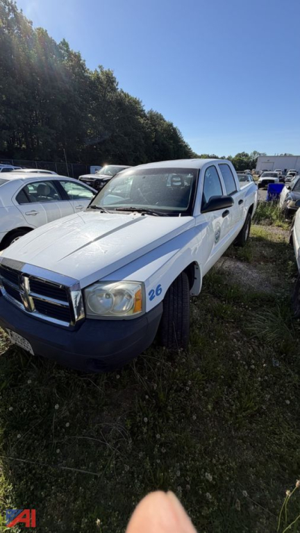 Dodge Dakota pickup truck in a used lot, white with blue accents, front left angle, number 26 on fender, outdoors with other vehicles in background.