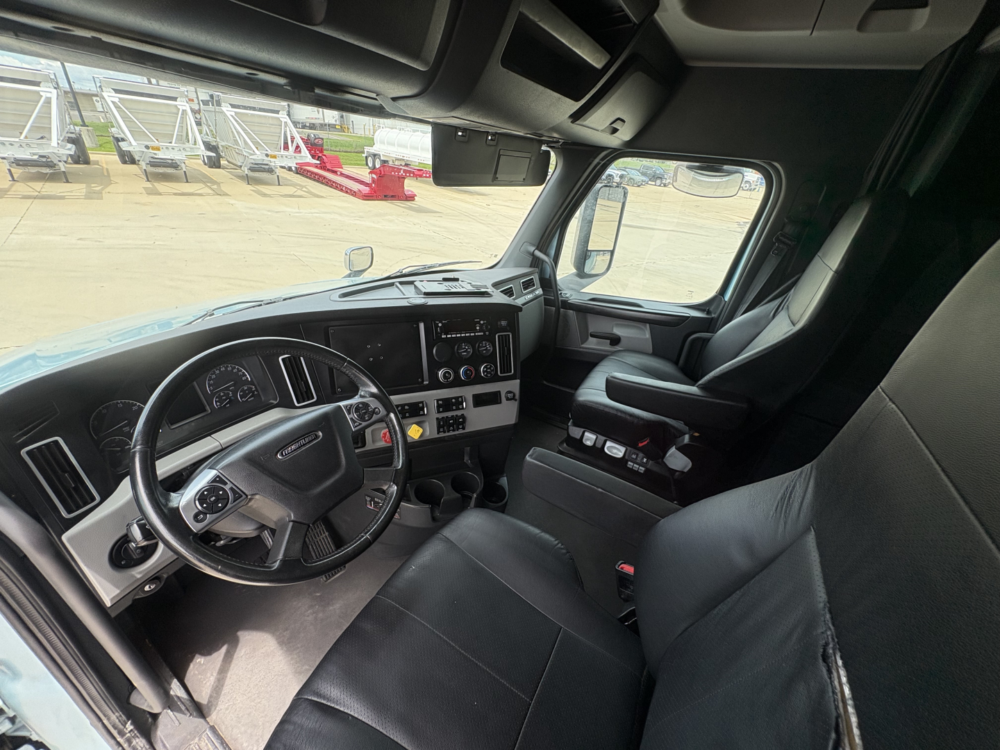 Freightliner Cascadia 126 cab interior showing steering wheel, dashboard, driver seat, and center console.