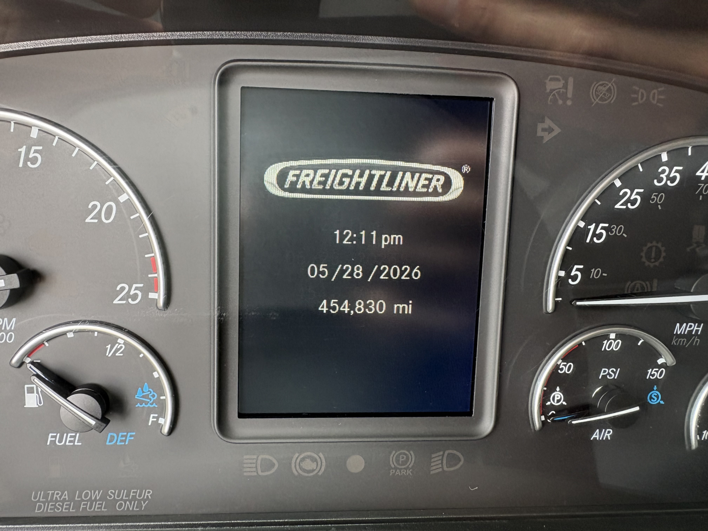 Dashboard display showing Freightliner logo with time 12:11 pm, date 05/28/2026, and 454,830 miles. Surrounding gauges include speedometer, fuel, DEF indicators.
