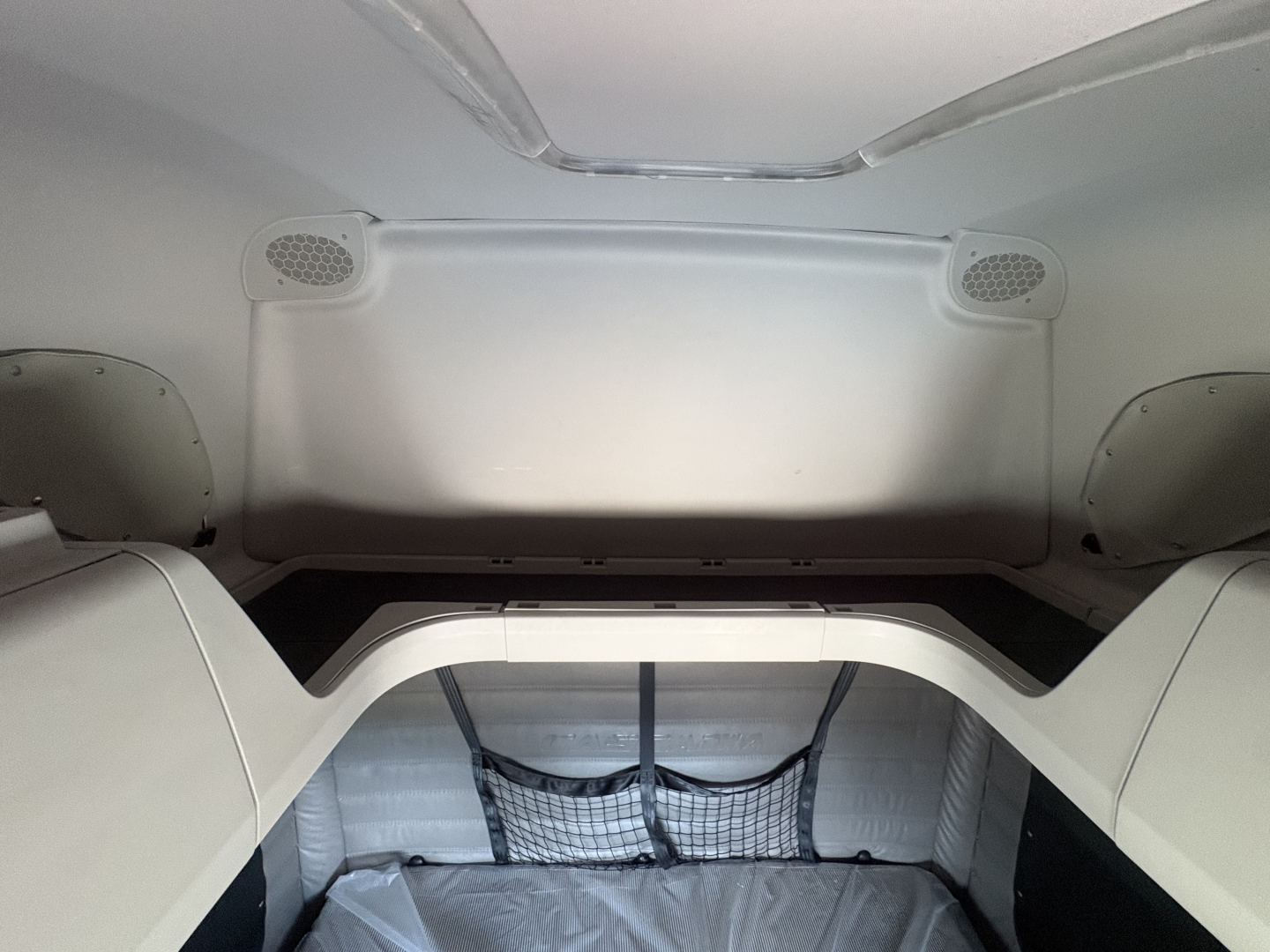 Truck cab interior showing sleeper area with light gray panels and cargo net in rear storage area.