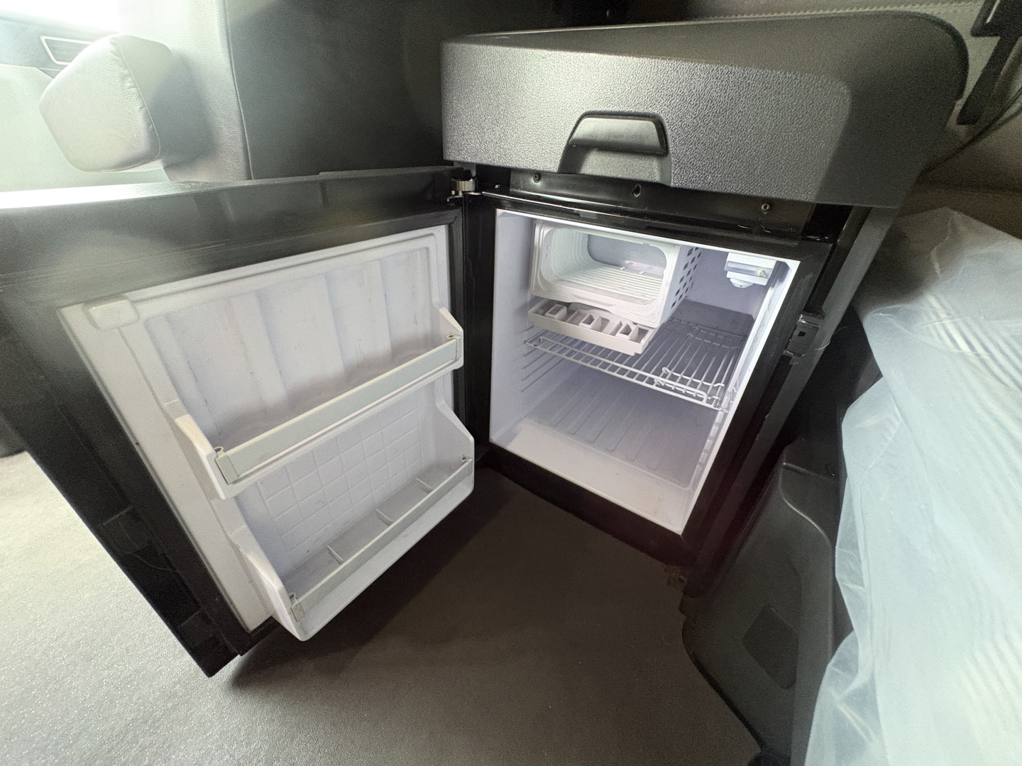 Mini fridge in Freightliner Cascadia truck cab showing open doors with empty freezer and refrigerator shelves.