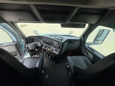 Cab interior of a Freightliner Cascadia 126 semi-truck showing dual front seats, steering wheel, dashboard with gauges and control panels.