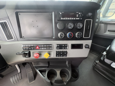 Dashboard interior of a Freightliner Cascadia 126 showing gauge cluster, stereo, hazard switch, and cup holders.