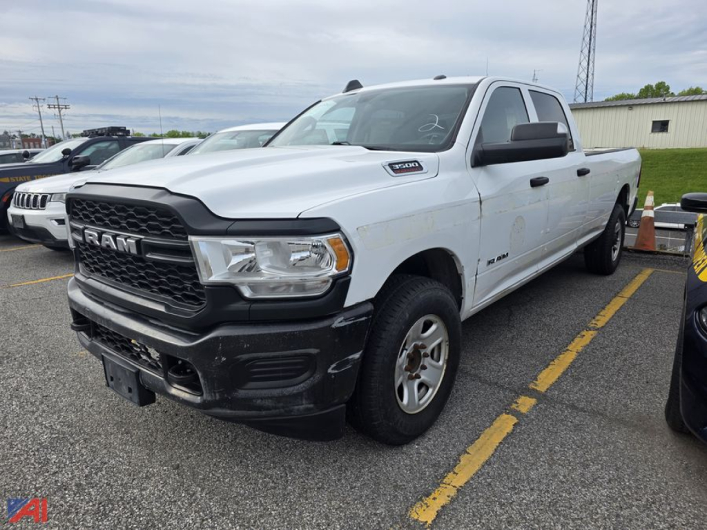 Ram 2500/3500 pickup truck in a parking lot showing front grille with RAM logo, white body, black bumper, crew cab, side badge near front fender, and grey steel wheels.