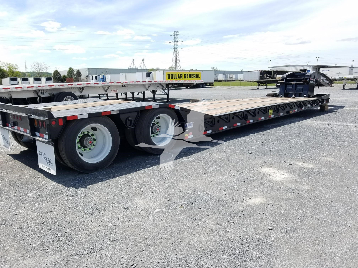 Lowboy trailer with multi-axle deck showing steel frame and wheels, DOT/brand decals visible, trailer bed extending into distance.