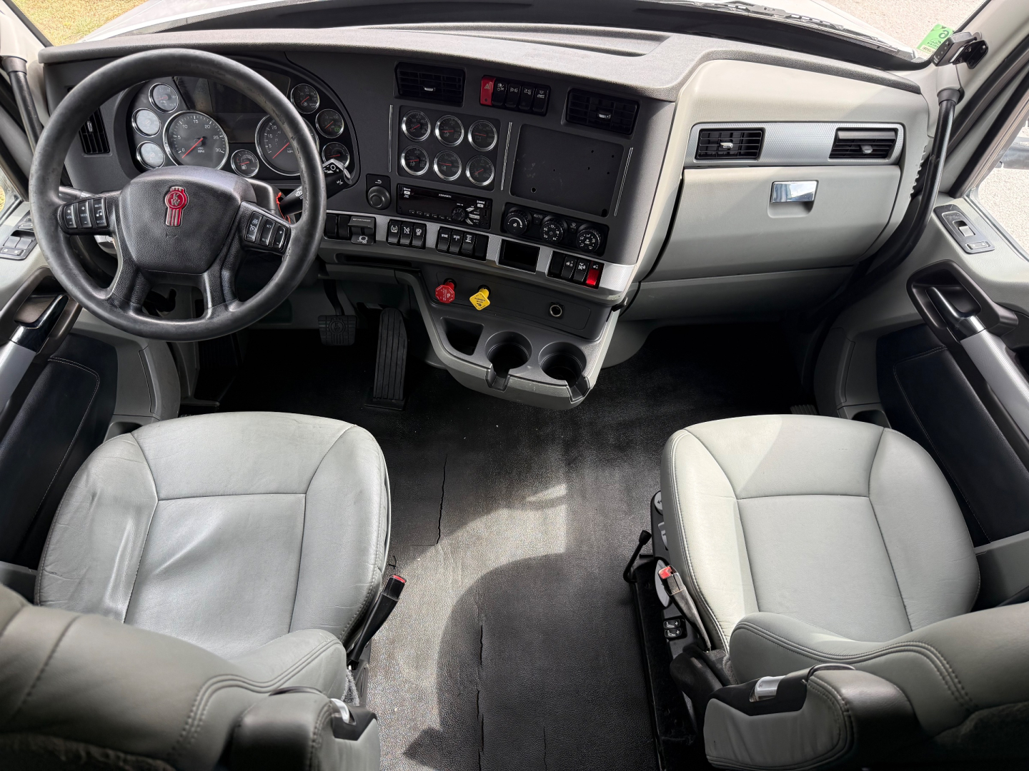 Truck cab interior of a 2020 Kenworth T680 showing steering wheel, dashboard with gauges, center console, and two gray seats.