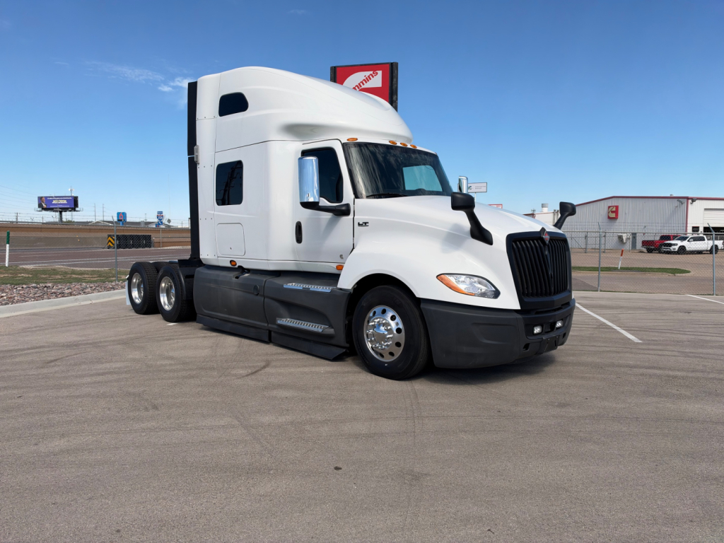 International LT625 semi-truck in a parking lot, white exterior, sleeper cab, three rear axles, front grille and headlights visible, no visible logos text.