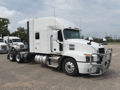 Truck cab in a parking lot showing a white 2023 Mack Anthem sleeper with chrome bumper guard and side fuel tanks.