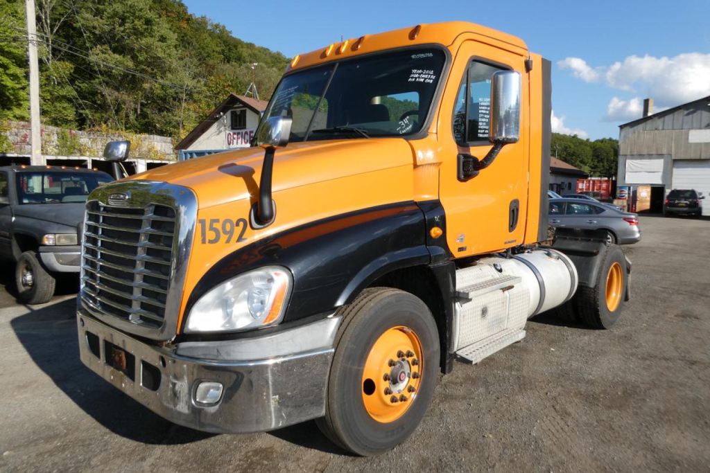 Truck cab view of a 2012 Freightliner Cascadia 125, orange and black color scheme, front grille, twin fuel tanks, number 1592 on door, parked lot.