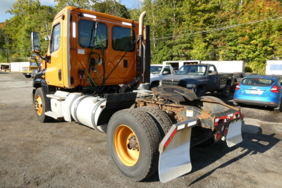 Orange Freightliner Cascadia 125 daycab chassis in view showing cab and rear tractor frame with mud flaps and dual rear wheels.