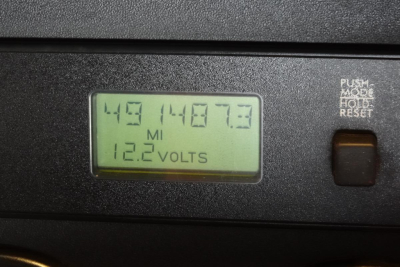 Digital display showing 49 miles? 14877.7 MI and 12.2 VOLTS with a push-to-hold reset button nearby.