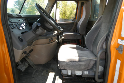 Truck cab interior of a 2012 Freightliner Cascadia 125 daycab showing driver seat, steering wheel, dashboard, and passenger seat.