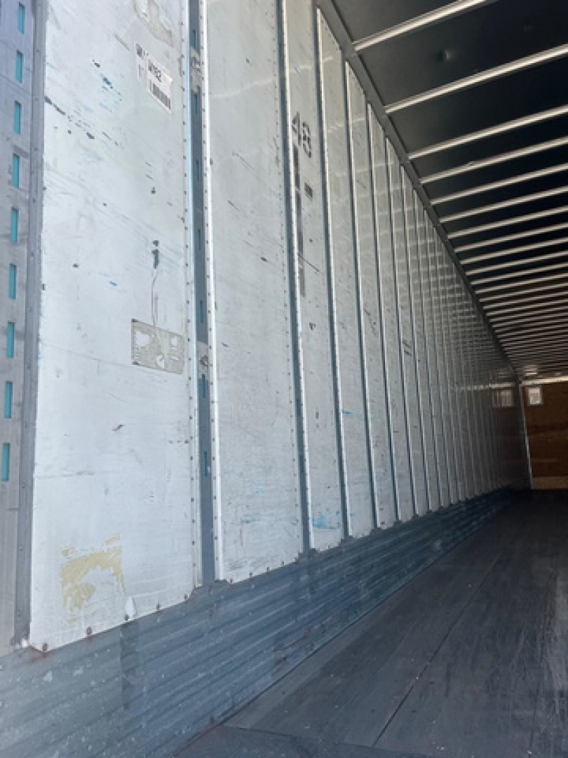 Interior of a trailer van showing aluminum side walls, ribbed metal structure, and wooden floor.