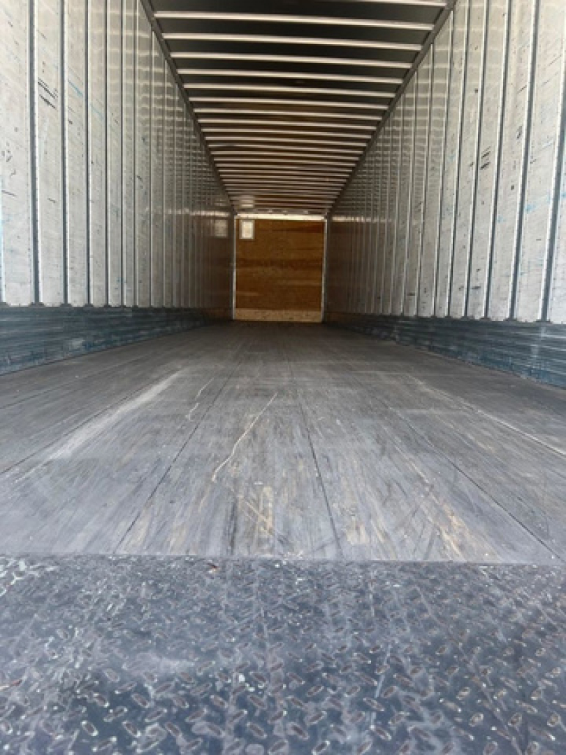 Interior of a trailer showing empty cargo space with wooden bulkhead at the far end. Rust-free steel walls with corrugated side panels and a diamond plate floor.