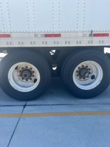 Dual rear trailer wheels under a 2012 Utility Van with riveted aluminum side panels and reflective stripes visible.