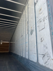 Trailer interior wall with metal panels and corrugated ceiling, empty cargo area, side wall panels with scuff marks.